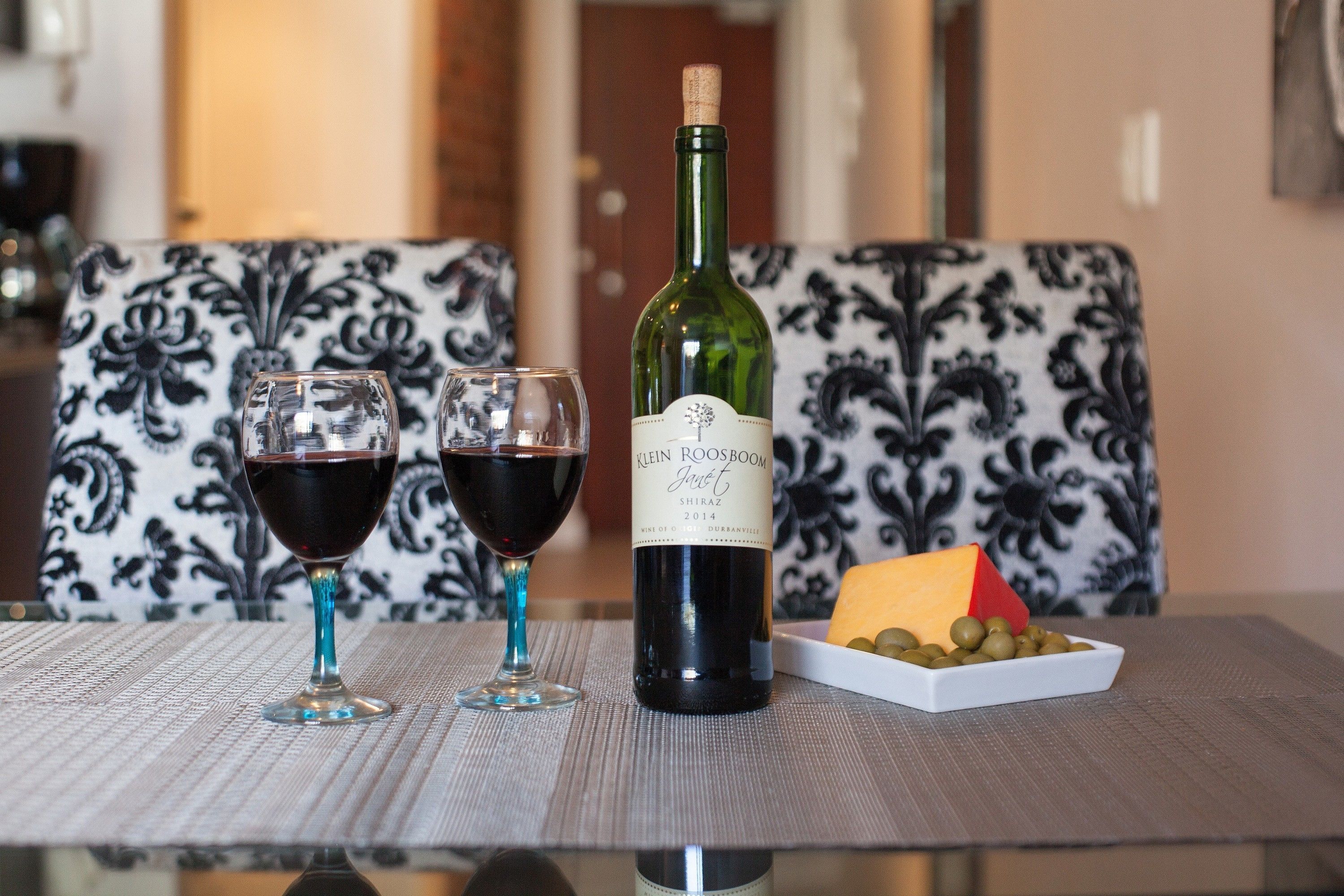 A table with two wine glasses, a bottle of wine, and a small dish of olives and cheese.