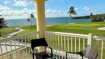 Un balcón con dos sillas y una mesa, con vista a un campo de golf y una extensión de agua.