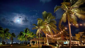 Un resort nocturno con palmeras, luces colgantes y un edificio con terraza.