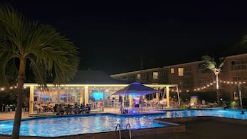Un espace piscine aménagé pour la nuit, avec un coin salon abrité et une scène.
