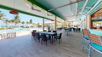 A poolside area with tables and chairs, a pool, and palm trees in the background.