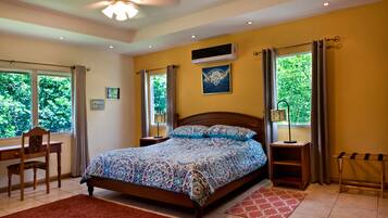 A bedroom with a bed, a desk, a chair, a window with curtains, an air conditioning unit, and a ceiling fan.