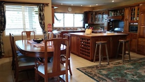 Una cocina con armarios de madera, una mesa de comedor con sillas, una barra y un ventanal con cortinas.