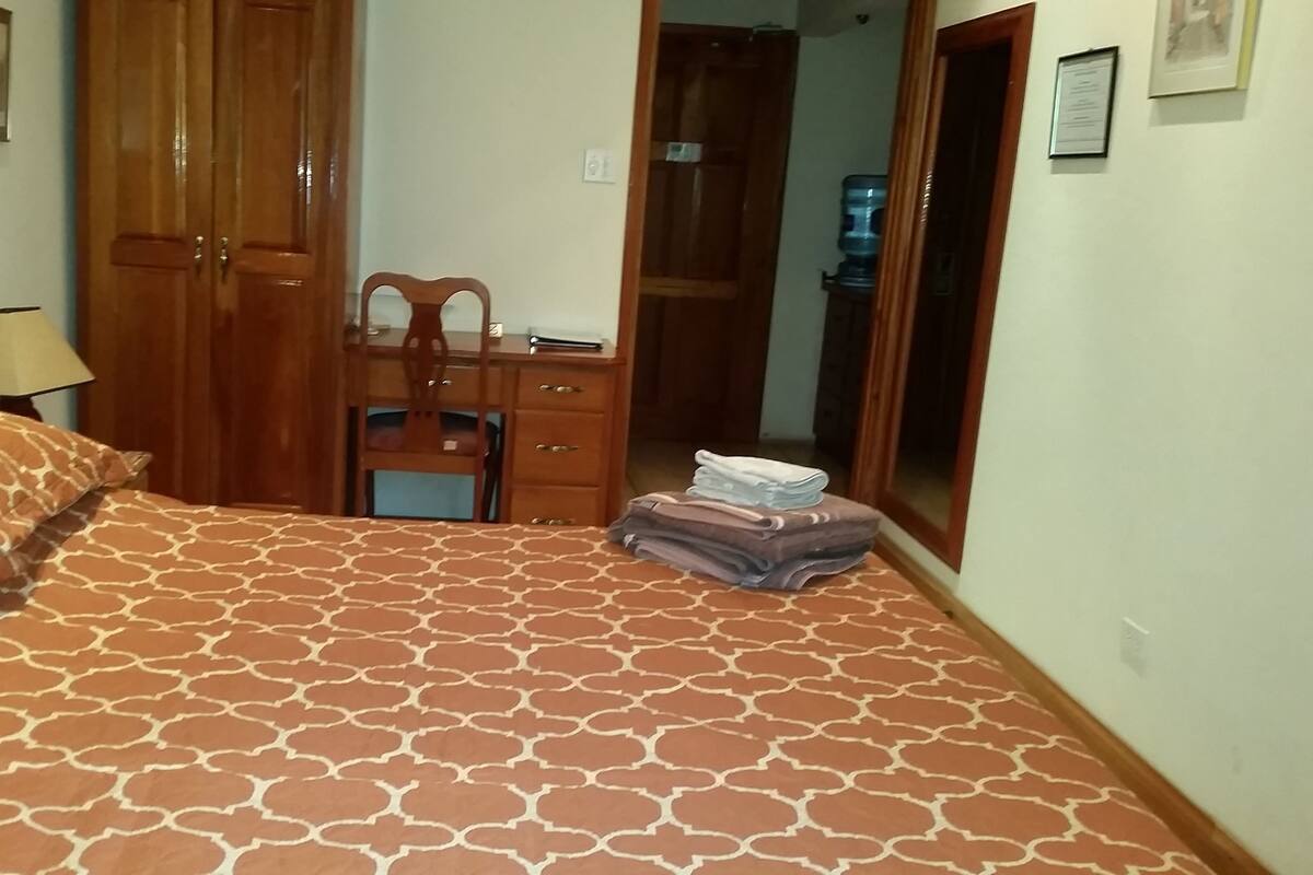 Ein Schlafzimmer mit einem Bett, einem Holzschrank, einem Schreibtisch mit Stuhl und einem Spiegel.