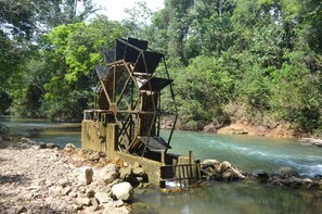 Una estructura rústica de noria junto a un río, rodeada de abundante vegetación.