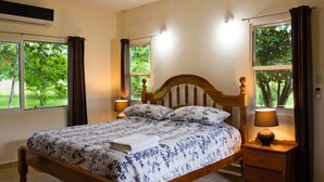 Un dormitorio con cama de madera, dos lámparas de noche, una mesita de noche y ventanas amplias con cortinas.