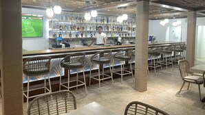 A bar area with a bartender, wicker chairs, and a shelf stocked with bottles. - Spindrift Hotel (San Pedro)