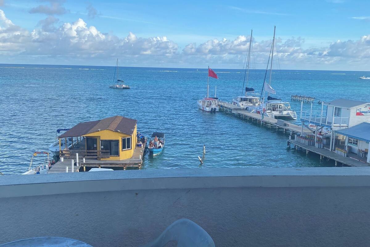 Vista desde un balcón sobre un puerto deportivo con barcos amarrados, un muelle y un edificio con una bandera roja.