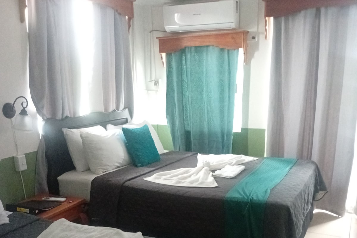 Una habitación de hotel con dos camas, una mesita de noche, una lámpara y un equipo de aire acondicionado.