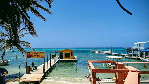 A dock extending into clear turquoise waters with a small yellow building, palm trees, and a sign for Spindrift Hotel Dock. - Spindrift Hotel (San Pedro)