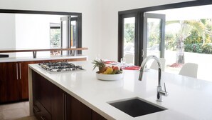 Una cocina moderna con una isla central, estufa a gas integrada, un fregadero y un bol de fruta.