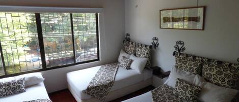 A room with two beds, each with patterned bedding and a headboard. There is a window with bars, and a framed picture on the wall.