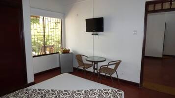 A room with a bed, a small table, two chairs, a TV mounted on the wall, and a window with bars.