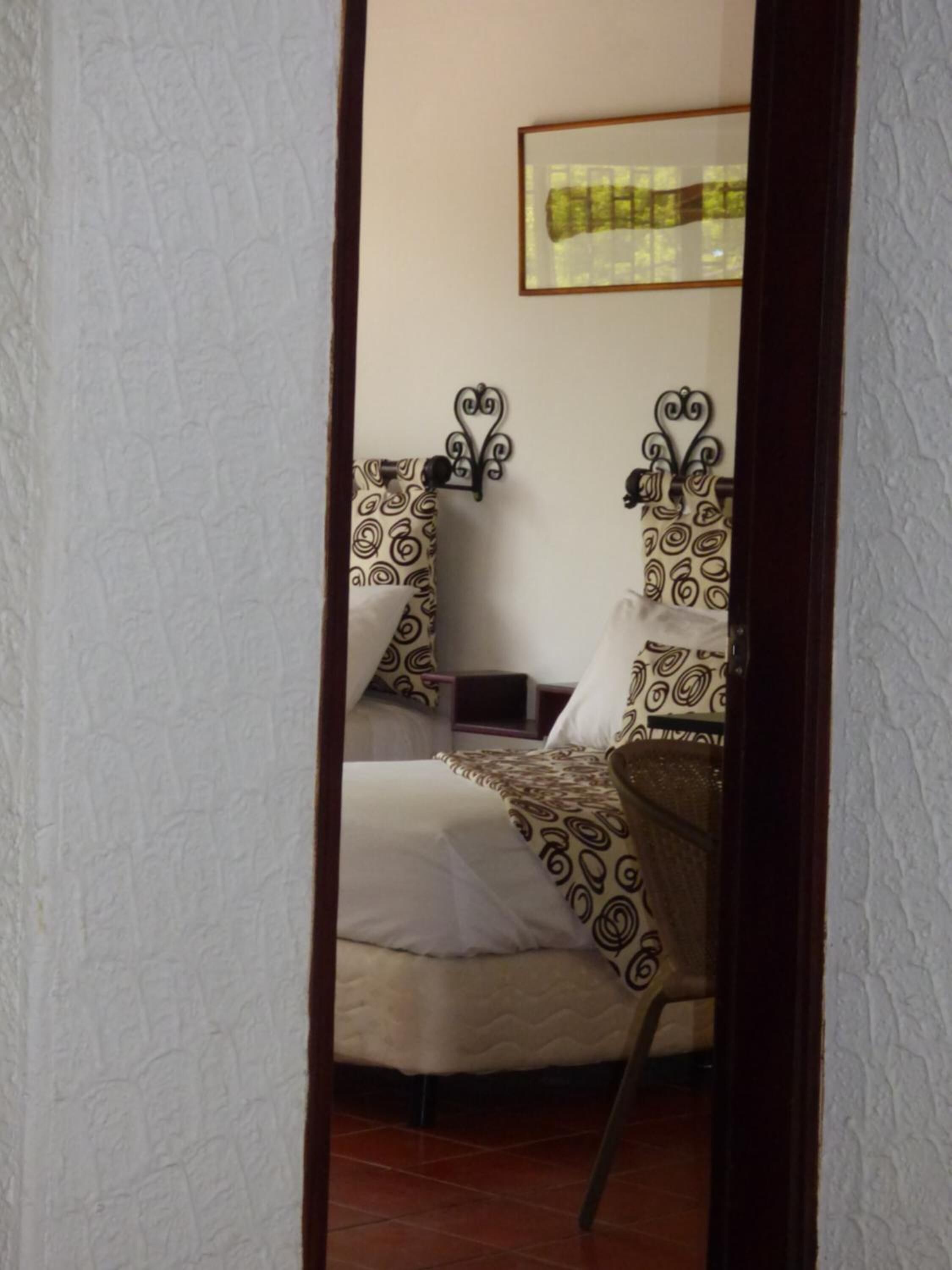 A single bed with a patterned bedspread and matching pillows, a headboard with a decorative design, and a framed picture on the wall above the bed.