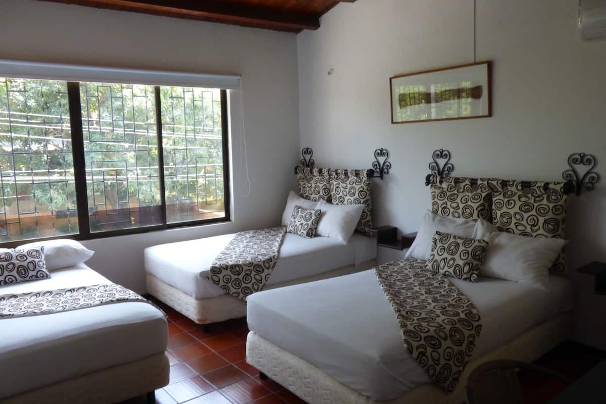 A hotel room with two beds, a large window with a view of greenery, and a framed picture on the wall.
