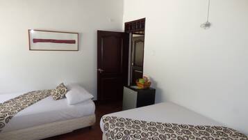 A hotel room with two single beds, a wooden door, a small table with snacks, and a framed picture on the wall.