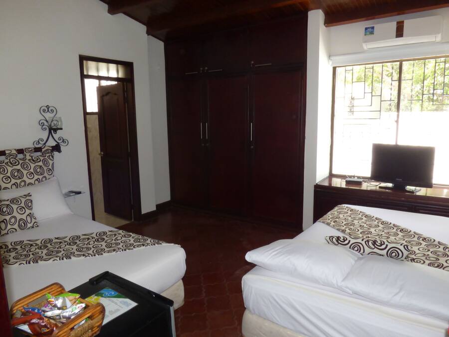 Habitación de hotel con dos camas, un armario, un televisor y una ventana con barrotes.