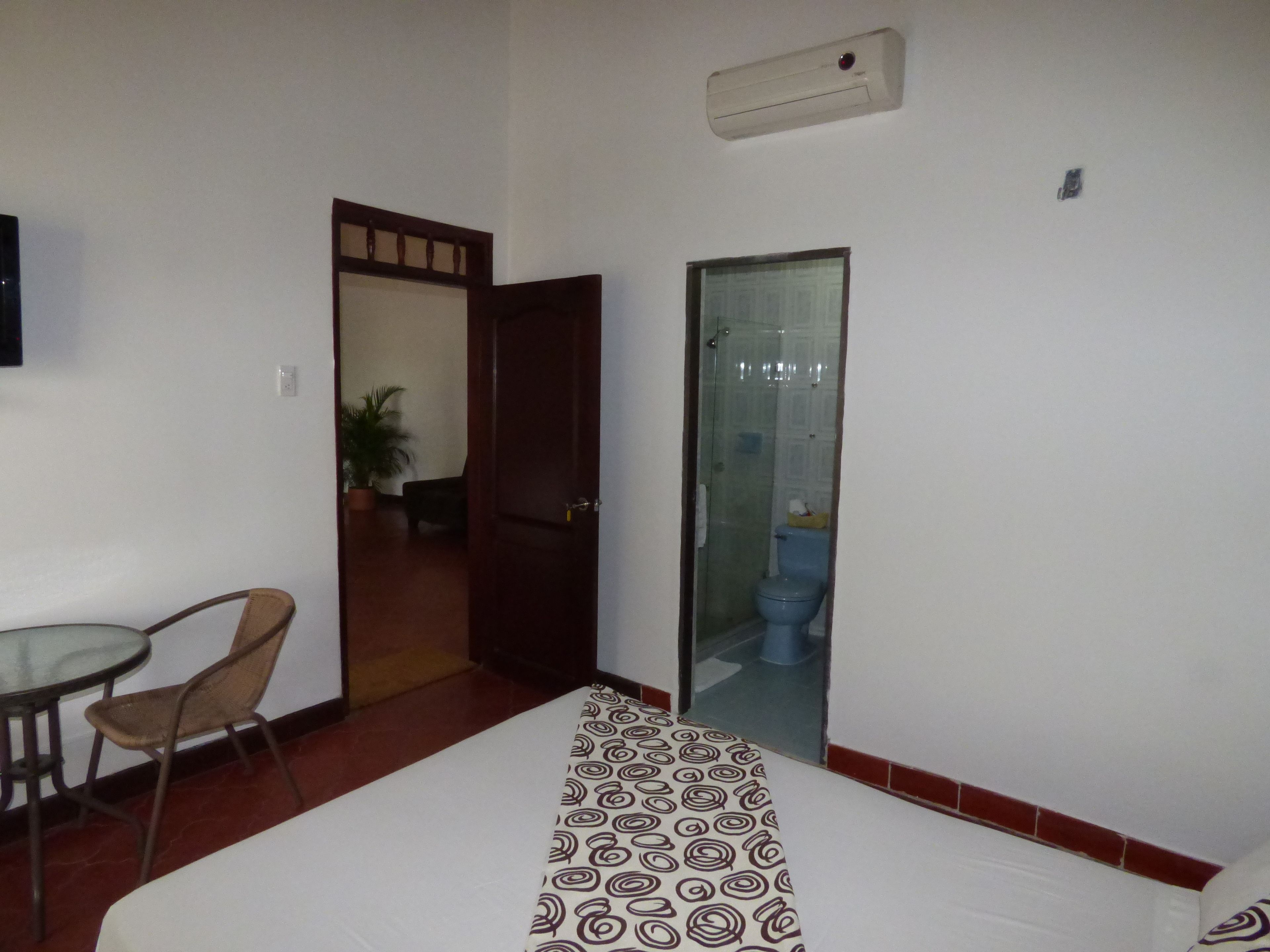 A hotel room with a bed, a small table, and a chair. There is a door leading to a bathroom with a toilet and a shower.