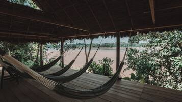 Relax in a hammock on a shaded deck overlooking the river, surrounded by lush greenery.