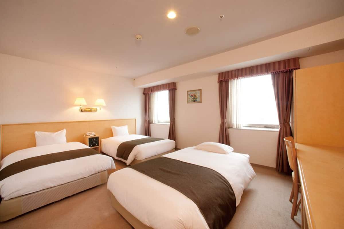 Ein Hotelzimmer mit zwei Betten, einem Schreibtisch, einer Lampe und einem Fenster mit Vorhängen.