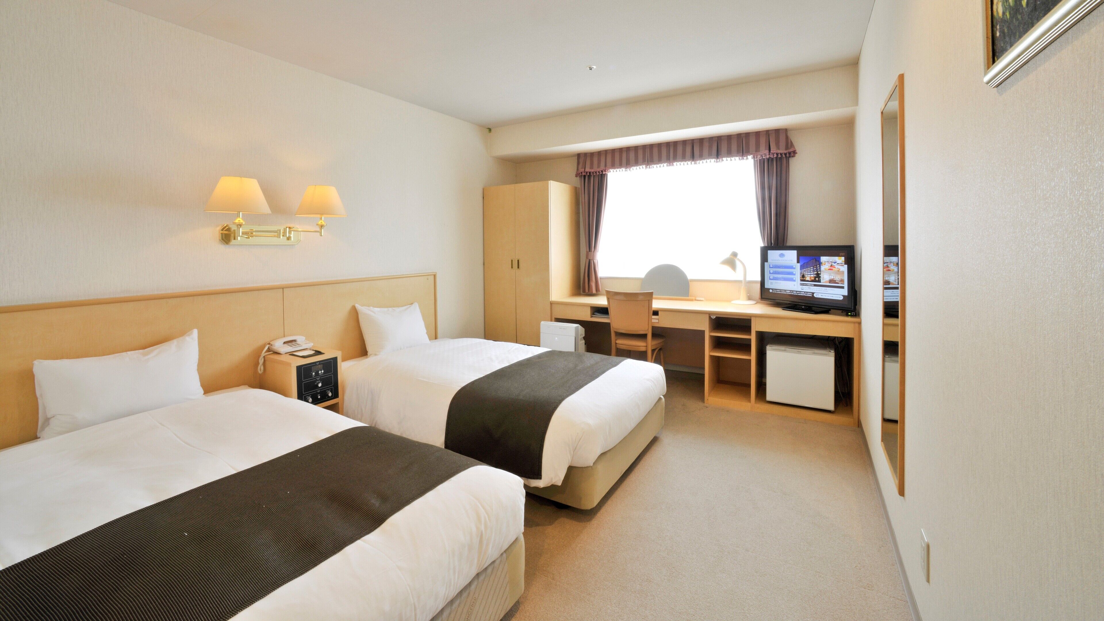 Ein Hotelzimmer mit zwei Betten, einem Schreibtisch, einem Stuhl, einem Fernseher und einem Fenster mit Vorhängen.