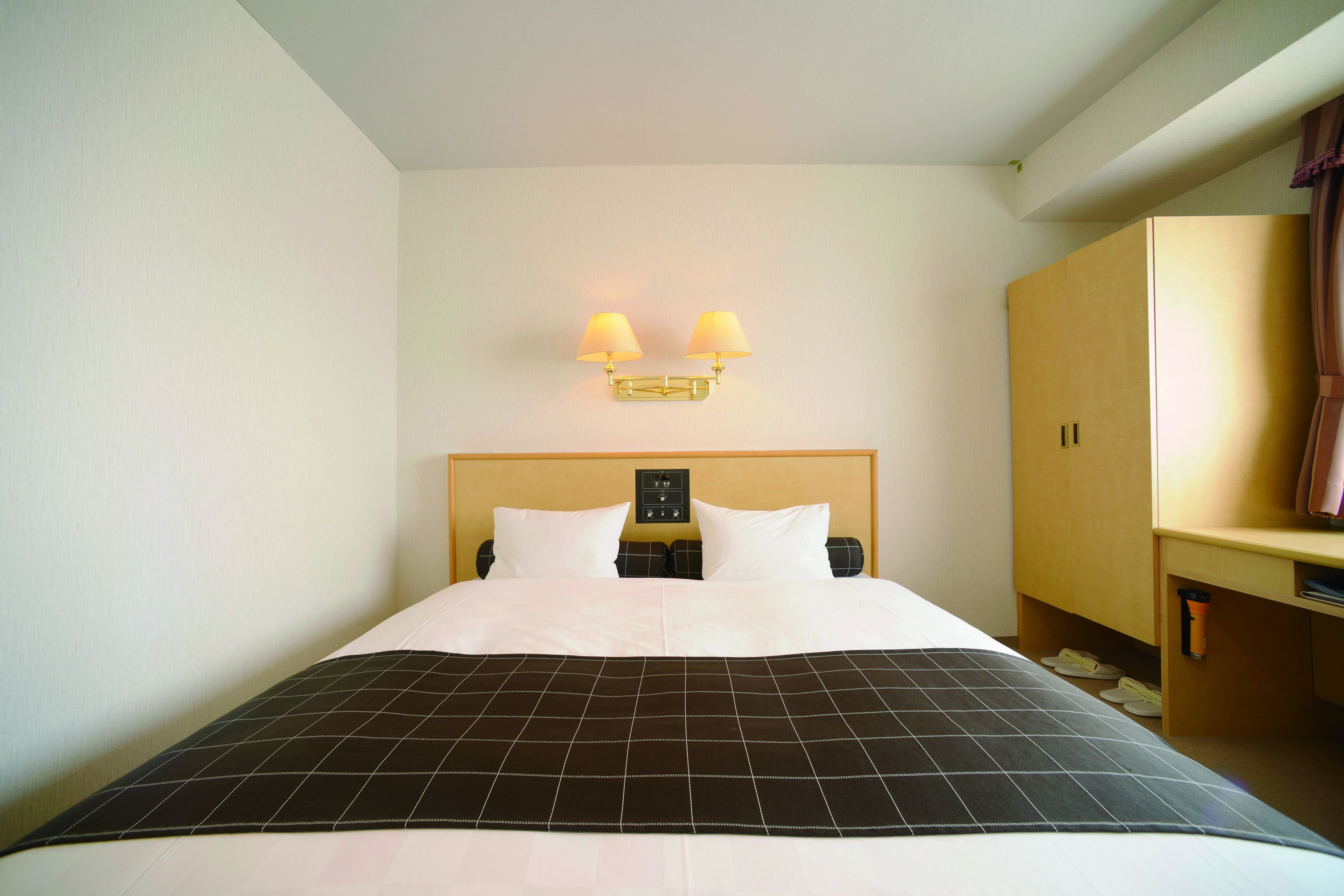 A hotel room with a bed, a nightstand, a lamp, and a wardrobe.