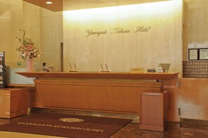 Un comptoir d’accueil avec un revêtement en bois, une enseigne au-dessus, et un espace d’accueil doté d’un tapis marron.