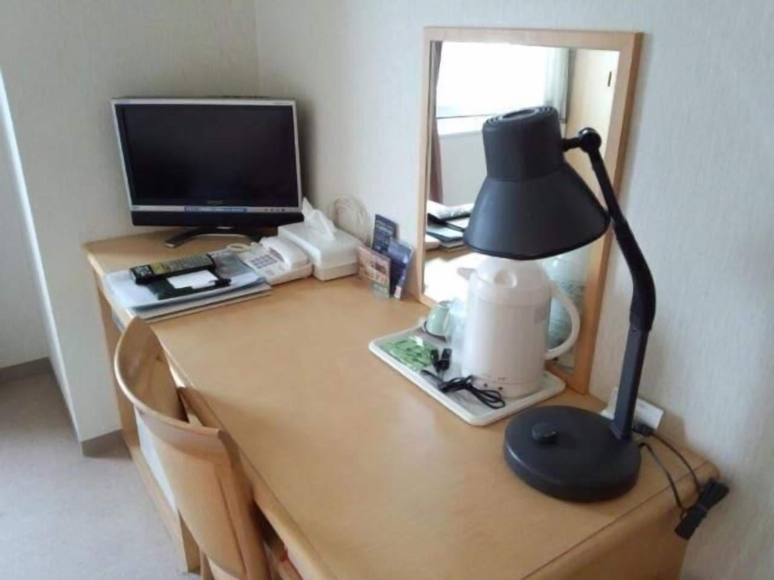 A hotel room desk with a computer monitor, telephone, lamp, and coffee maker.