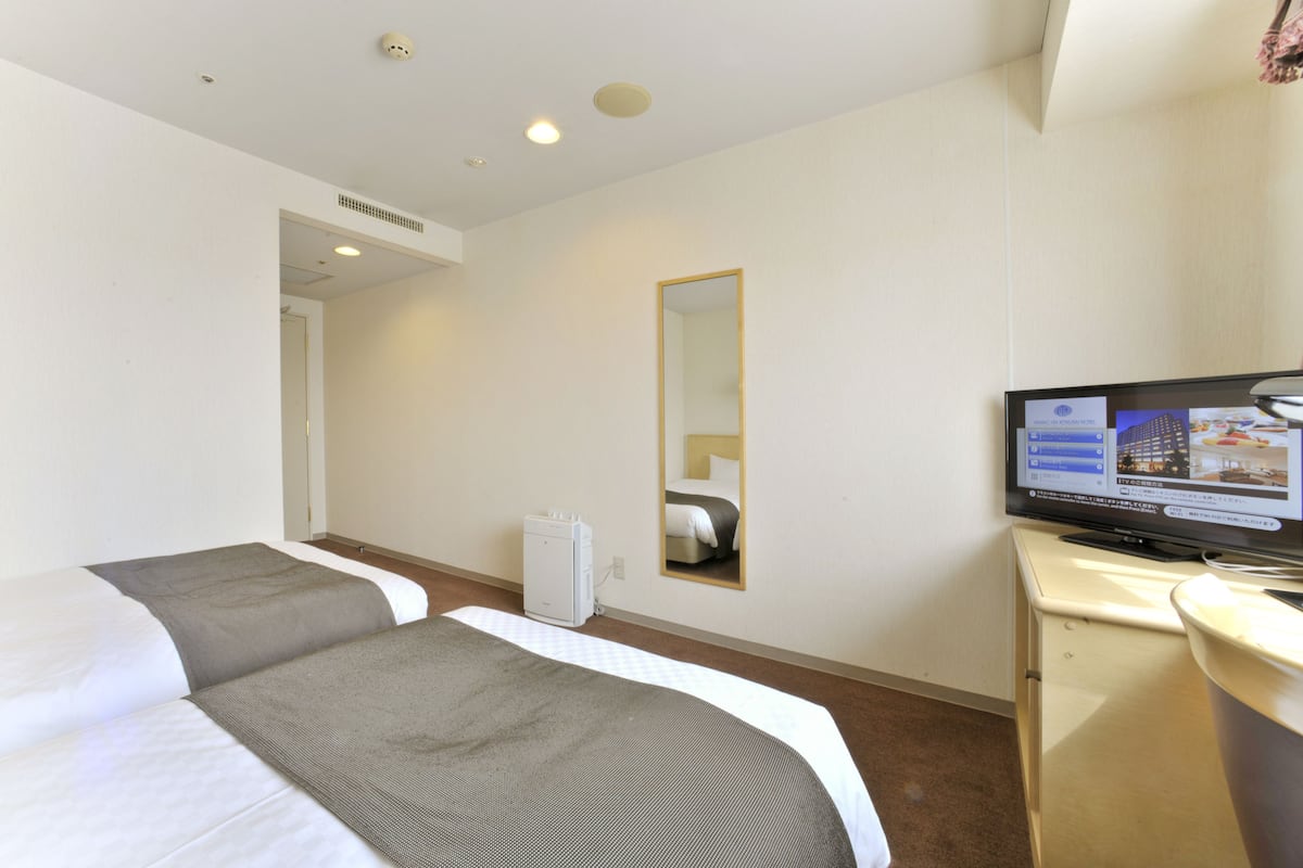 Une chambre d’hôtel avec deux lits, une télévision, un miroir et un bureau.