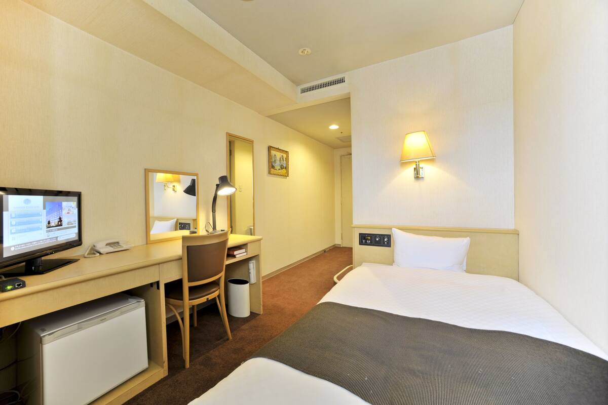 Une chambre d’hôtel équipée d’un lit, d’un bureau, d’une chaise, d’un ordinateur et d’un petit réfrigérateur.