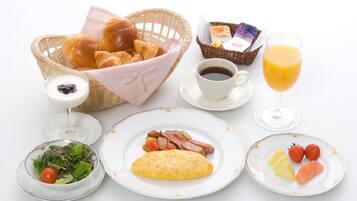 Un desayuno con cruasanes, una cesta de pan, un vaso de zumo de naranja, una taza de café, un plato con jamón y huevos, un bol de ensalada y un plato con fresas y piña.