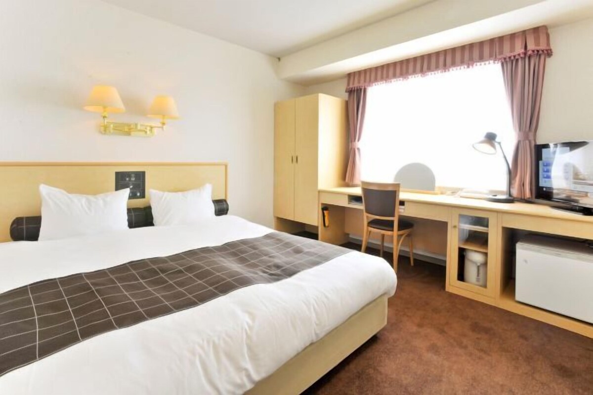 Ein Hotelzimmer mit Bett, Schreibtisch, Stuhl und einer kleinen Küchenzeile.
