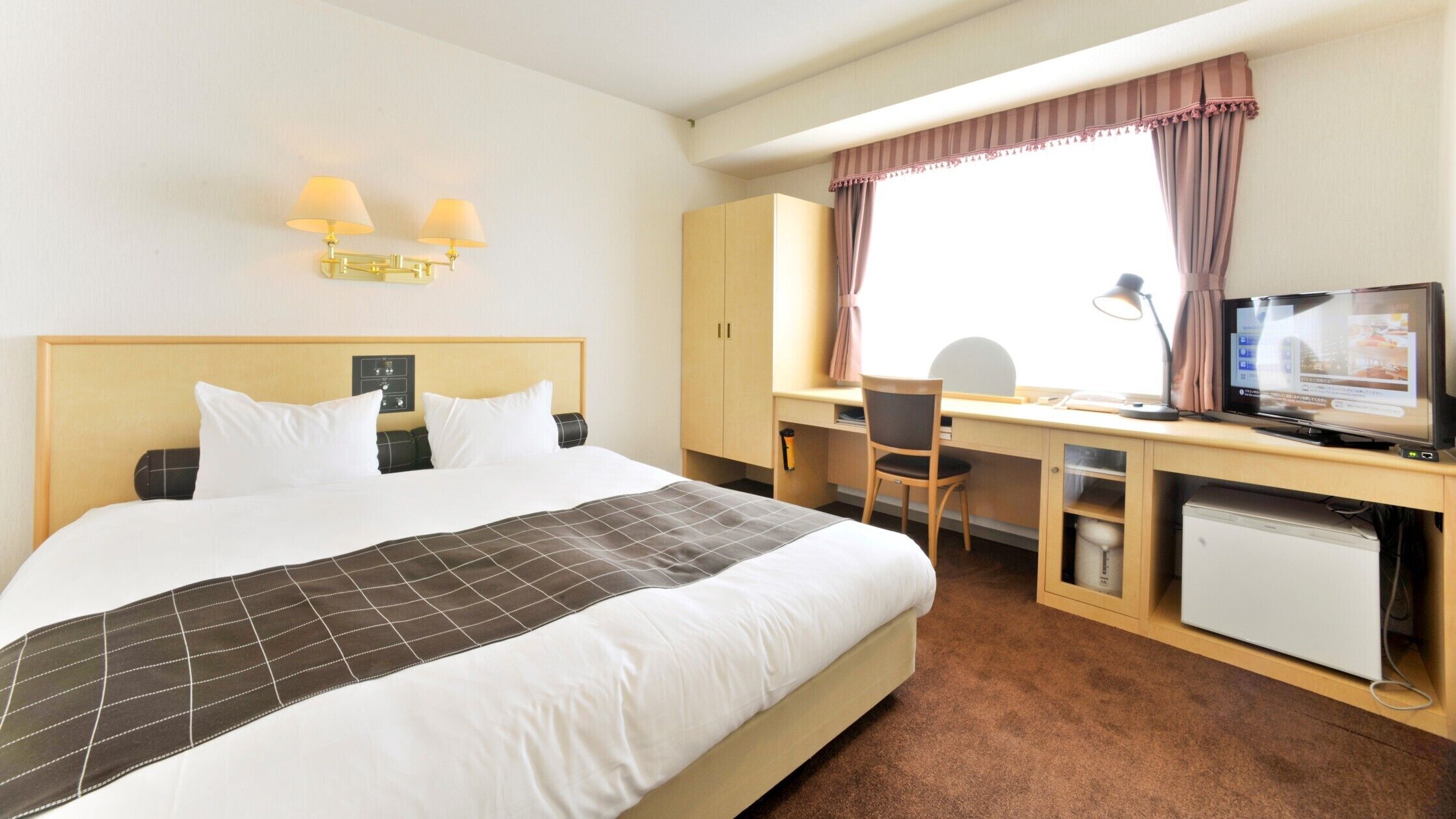 Une chambre d’hôtel équipée d’un lit, d’un bureau, d’une chaise, d’une télévision et d’un petit réfrigérateur.