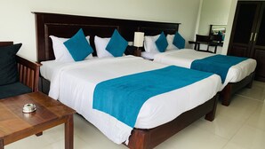 A hotel room with two beds, a wooden nightstand, a table, and a mirror. - Hotel Gangaaddara (Kandy)