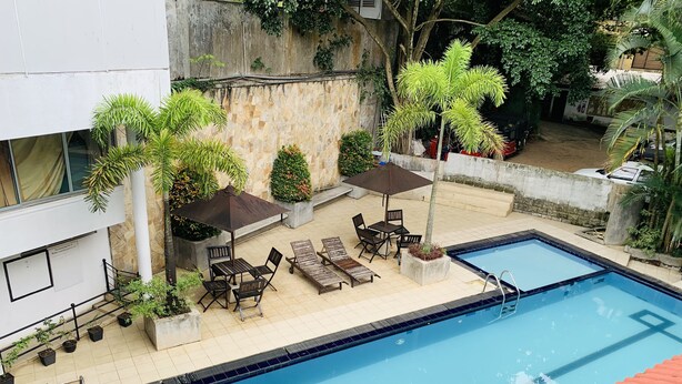 A swimming pool with a tiled deck, surrounded by potted plants and outdoor furniture. - Hotel Gangaaddara (Kandy)