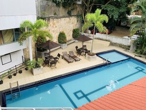 Una piscina con solárium empedrado, rodeada de macetas con plantas y mobiliario de exterior.