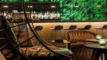 Una zona de bar con pared verde, sillones de cuero y barra con botellas.