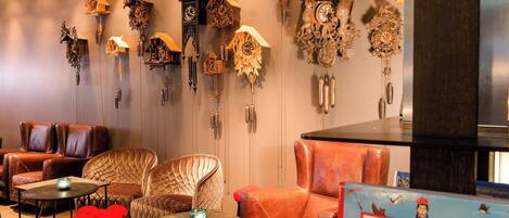 A room with leather sofas, a round table, and a wall adorned with various cuckoo clocks.