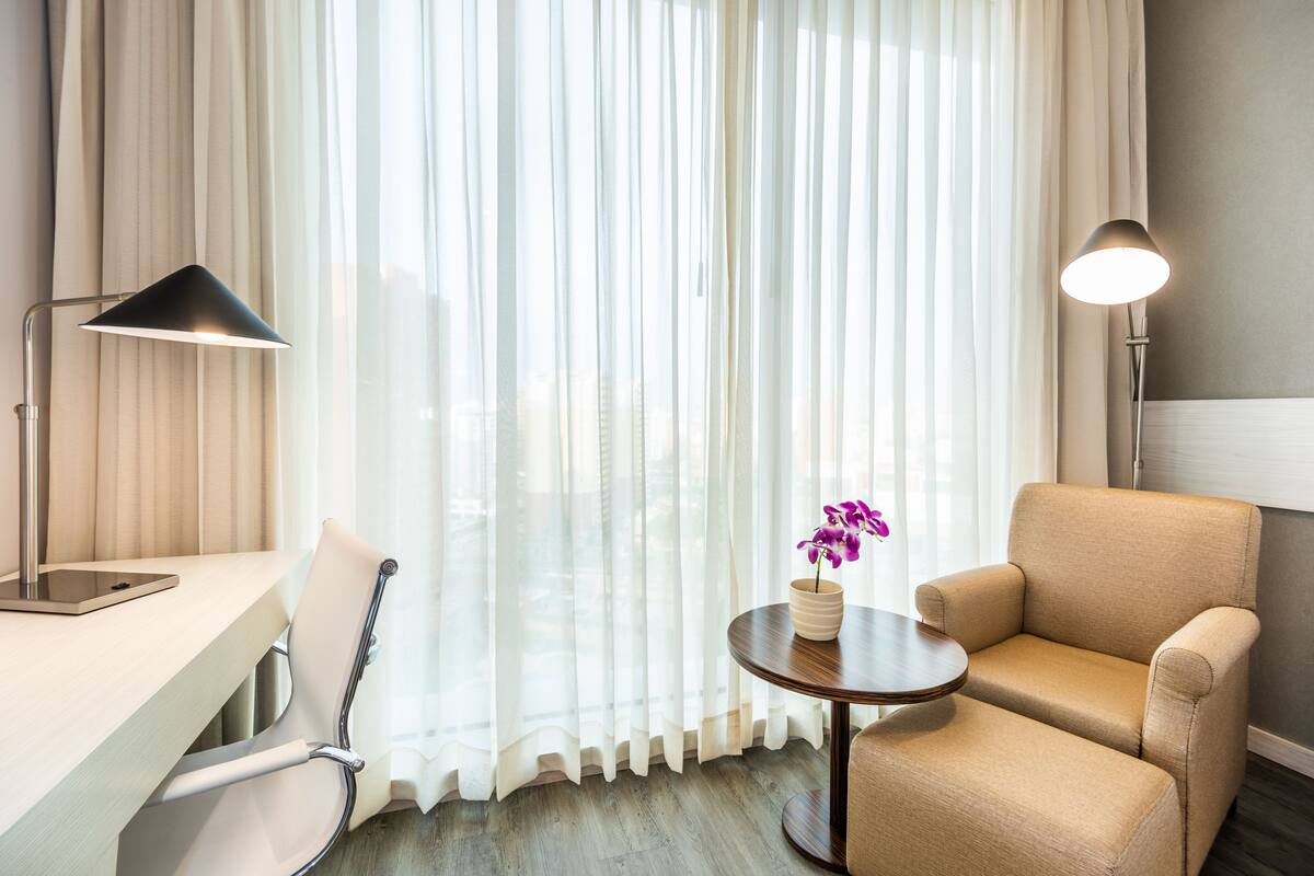 Une chambre d’hôtel équipée d’un bureau, d’une chaise, d’une lampe et d’une petite table sur laquelle est posé un vase de fleurs.