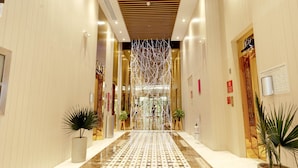 Vestíbulo de hotel con piso de baldosas, plantas en macetas e instalación de luces decorativas.