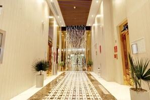 Een hotel lobby met een betegelde vloer, potplanten en een decoratieve lichtinstallatie.