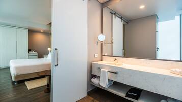 Ett modernt hotellrum med en säng, ett badrum med en stor spegel, ett handfat och en handduksställning.