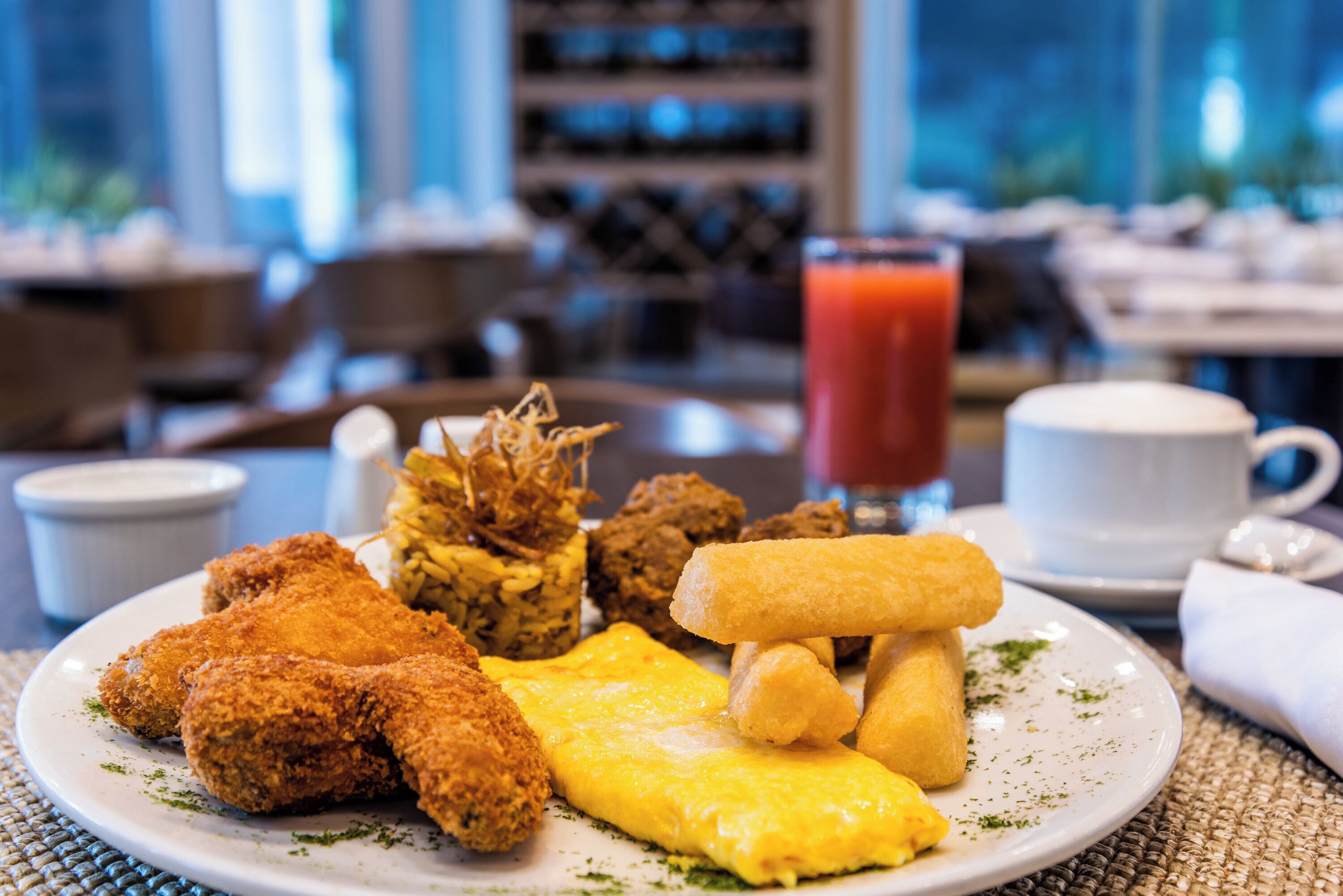 A plate of food including fried items, a slice of omelette, and a glass of red drink.