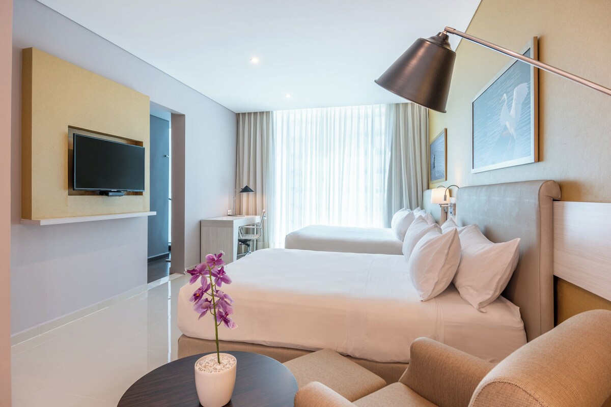 Een hotelkamer met een bed, een bureau, een televisie, een lamp en een vaas met bloemen.