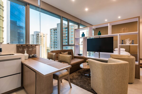 Een moderne woonkamer met een bank, stoelen, een televisie en een keukenhoek.