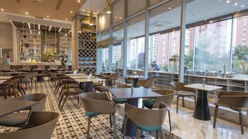 Un restaurante moderno con suelo de cuadros, varias zonas de estar y amplios ventanales con vistas a la ciudad.