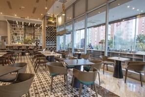 Een modern restaurant met een zwart-wit geruite vloer, meerdere zithoeken en grote ramen met uitzicht op de stad.