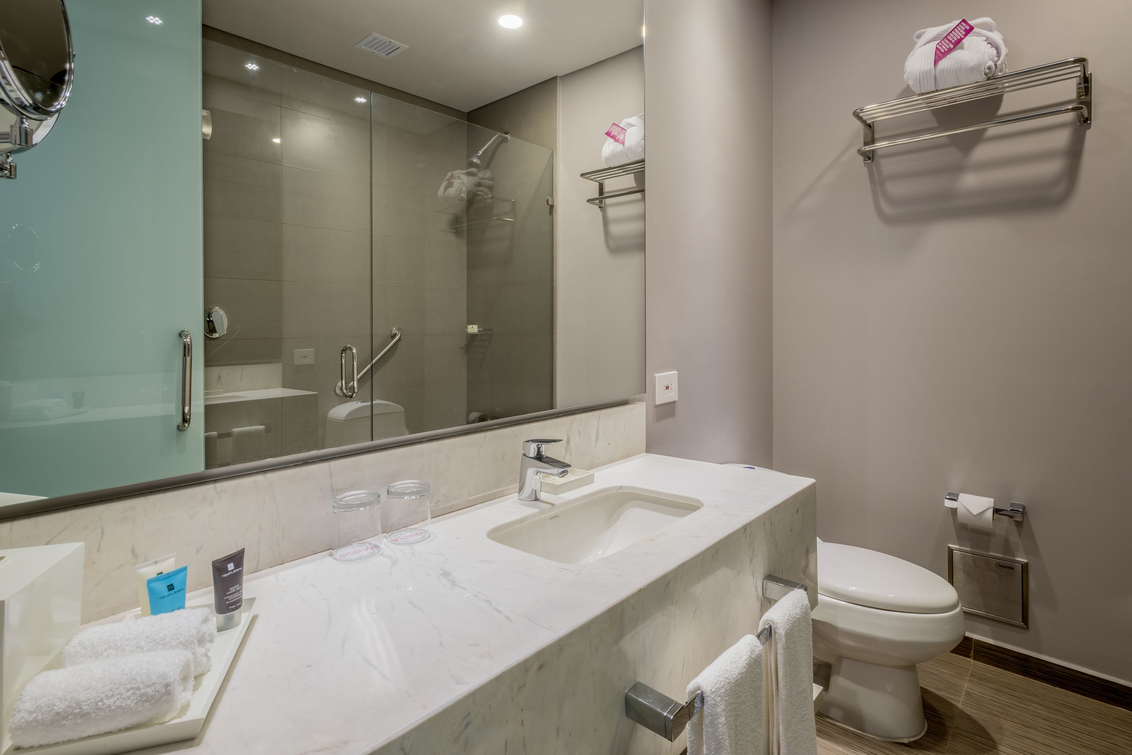 Un baño moderno con lavamanos de mármol, cabina de ducha con paredes de vidrio, inodoro y toallero.