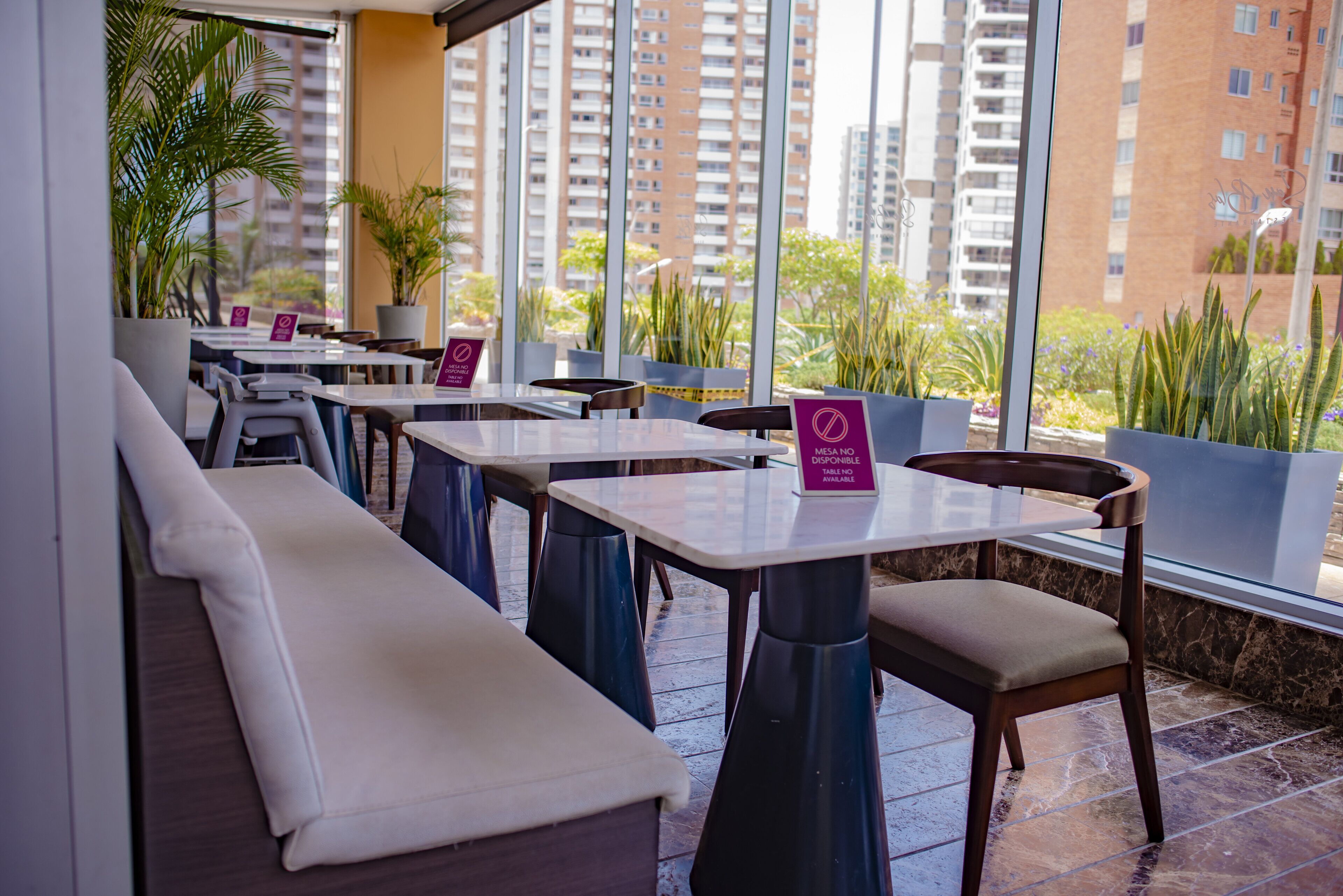 Un restaurante con terraza, amplios ventanales y plantas en macetas.