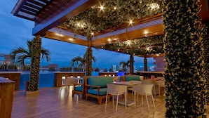 An outdoor seating area with wooden tables and chairs, surrounded by greenery and a view of the ocean. - Crowne Plaza Barranquilla by IHG (Barranquilla)